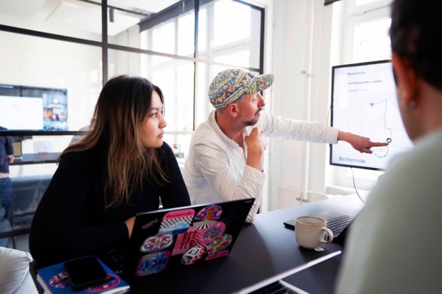 Work team in office meeting analyzing charts on screen and project data on laptop.