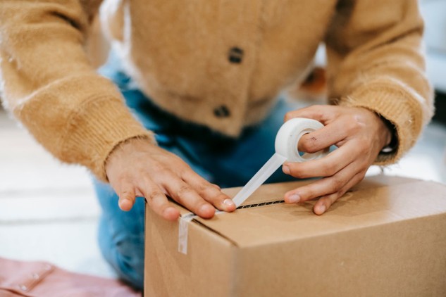 Person sealing a cardboard box with tape to prepare a parcel for shipping