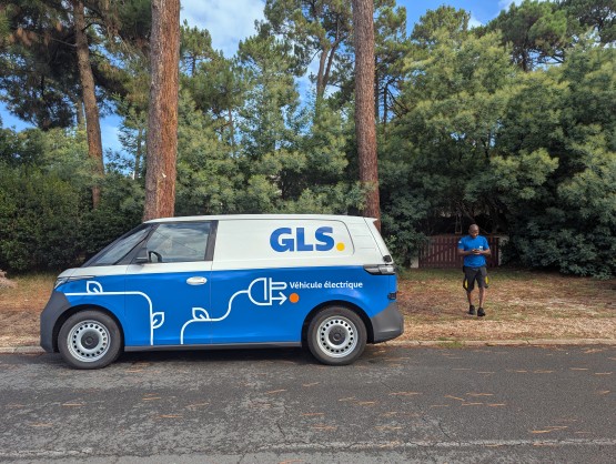 Camionnette de livraison électrique GLS marquée « Véhicule électrique », avec un livreur consulte son terminal, en milieu naturel.
