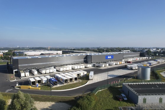 Vue aérienne d'un hub logistique GLS avec entrepôt, quais de chargement et flotte de camions et semi-remorques sur le parc.