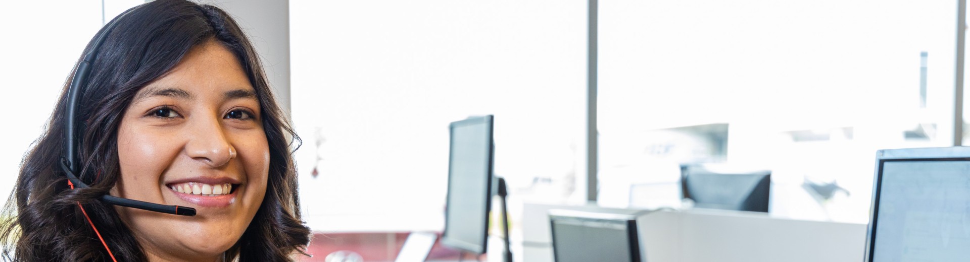 Smiling customer support agent wearing a headset at a computer.