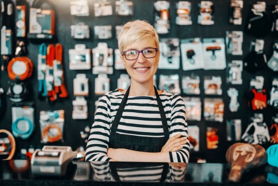 A woman stands in her storefront with her arms crossed, smiling.