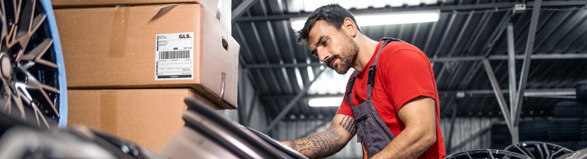 A warehouse worker inspects automotive parts beside stacked shipping boxes.